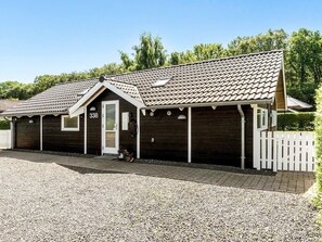 A wooden building with a tiled roof, a white picket fence, and a gravel driveway. - 5 Star Holiday Home in Juelsminde (Horsens)