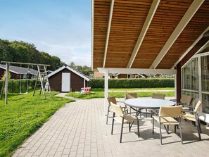 Un patio techado con una mesa redonda y sillas, un conjunto de columpios y un cobertizo pequeño.