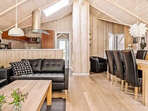 Un interior moderno con techo de madera, un sofá de cuero negro, un comedor con sillas y una cocina con armarios de madera.