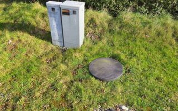A grassy area with two electrical boxes and a circular object.