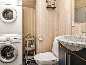 Un baño pequeño con lavadora, inodoro, estante con planta y lavamanos de granito.