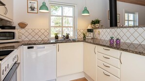 Una cocina moderna con armarios blancos, microondas, lavavajillas y estufa. Hay dos lámparas colgantes, una ventana y una planta en maceta sobre la encimera.