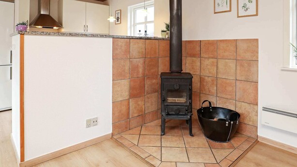 Una cocina con estufa de leña, armarios blancos y salpicadero de azulejos.