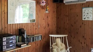 Ein Zimmer mit Holzwänden, einem weißen Stuhl, einem roten Tisch und einem Regal mit Büchern und elektronischen Geräten.