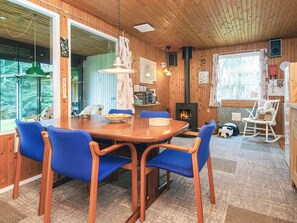 A cozy cabin interior with a wooden dining table, blue chairs, a fireplace, and a large window offering a view of the outdoors. - Cozy Holiday Home in Jutland near Lake (Silkeborg)