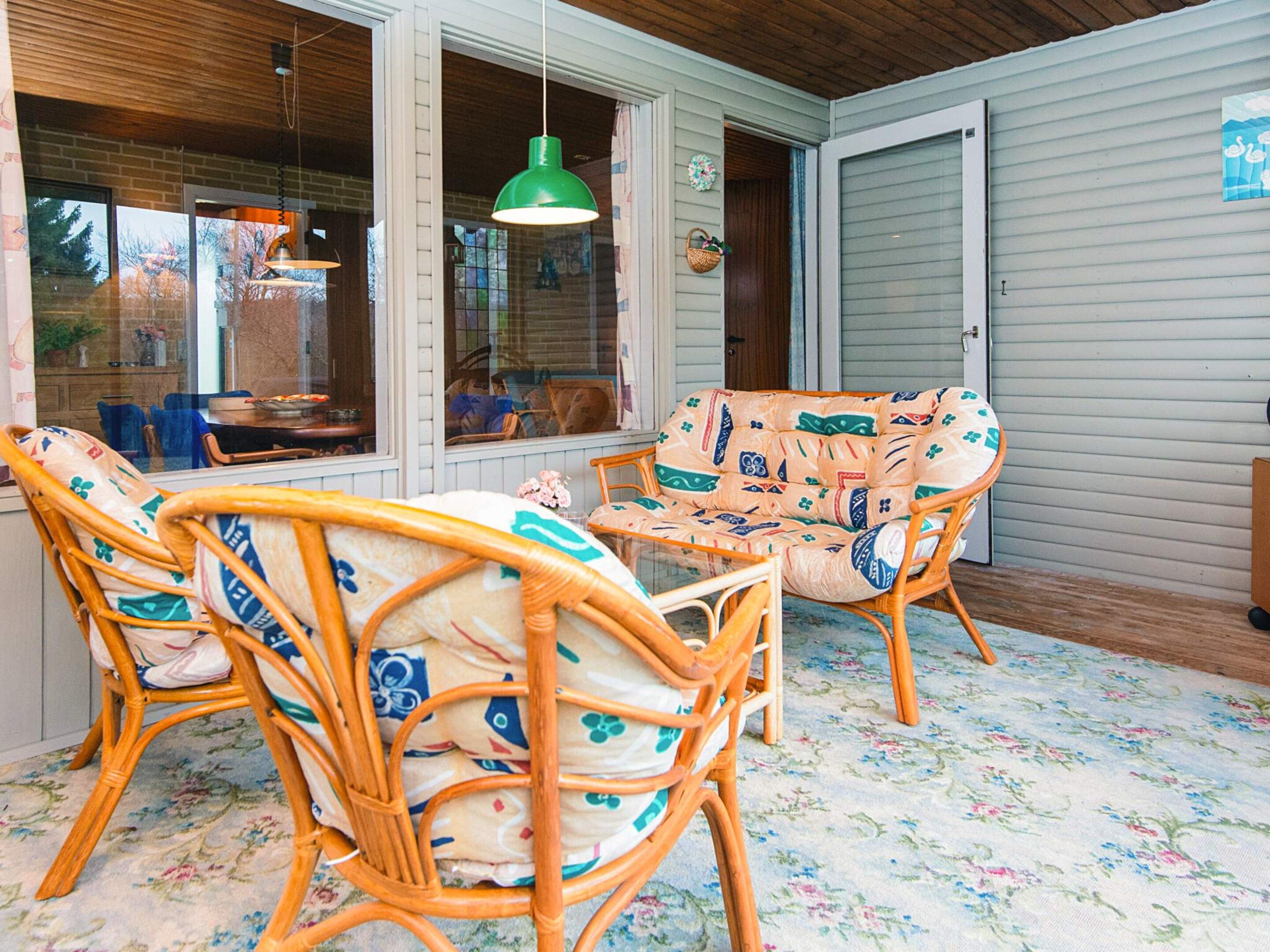 A room with wicker furniture, a green hanging light, and a window with a view of trees.