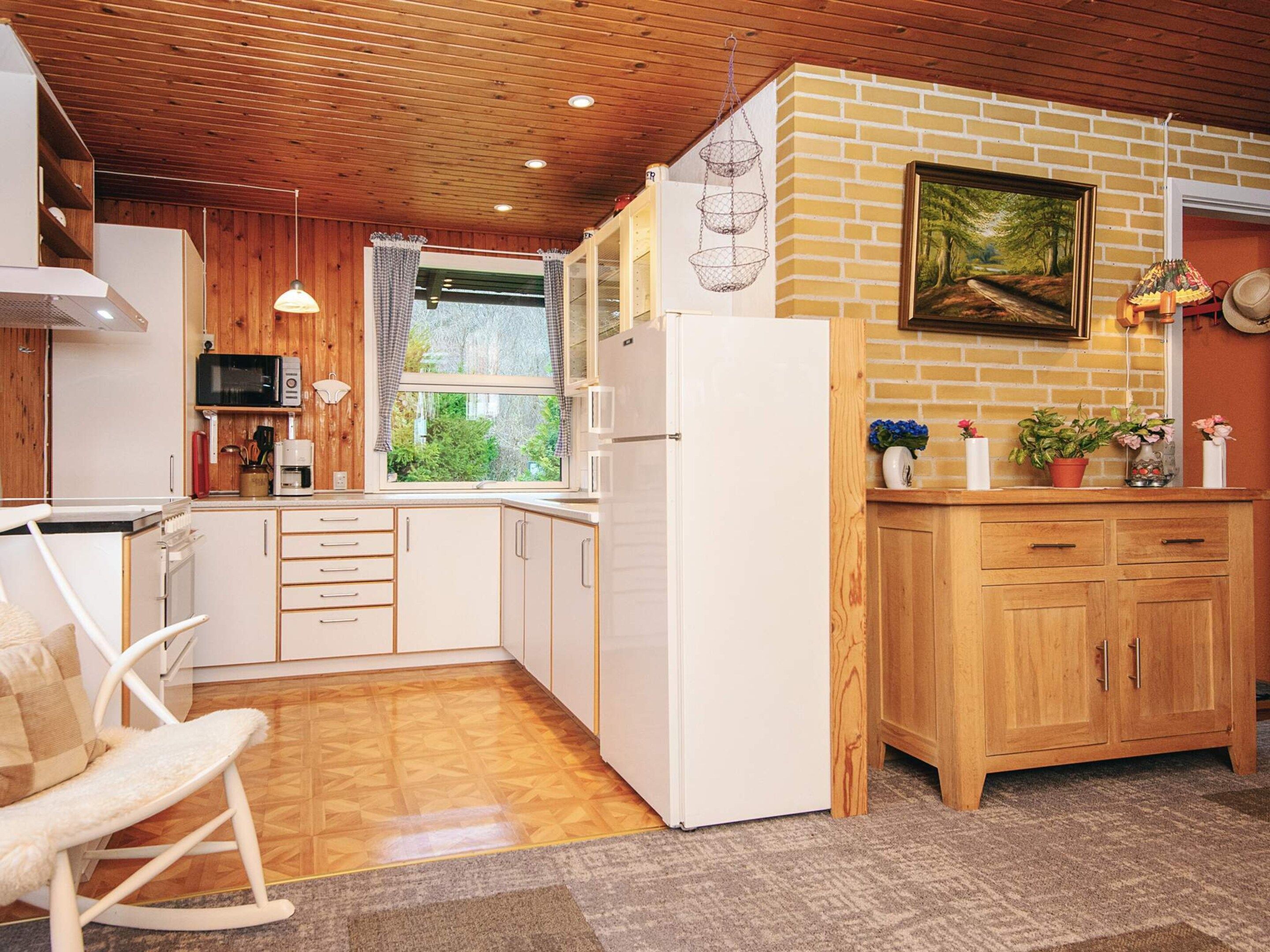 Cozinha compacta com eletrodomésticos brancos, armários de madeira e janela com vista para o verde.