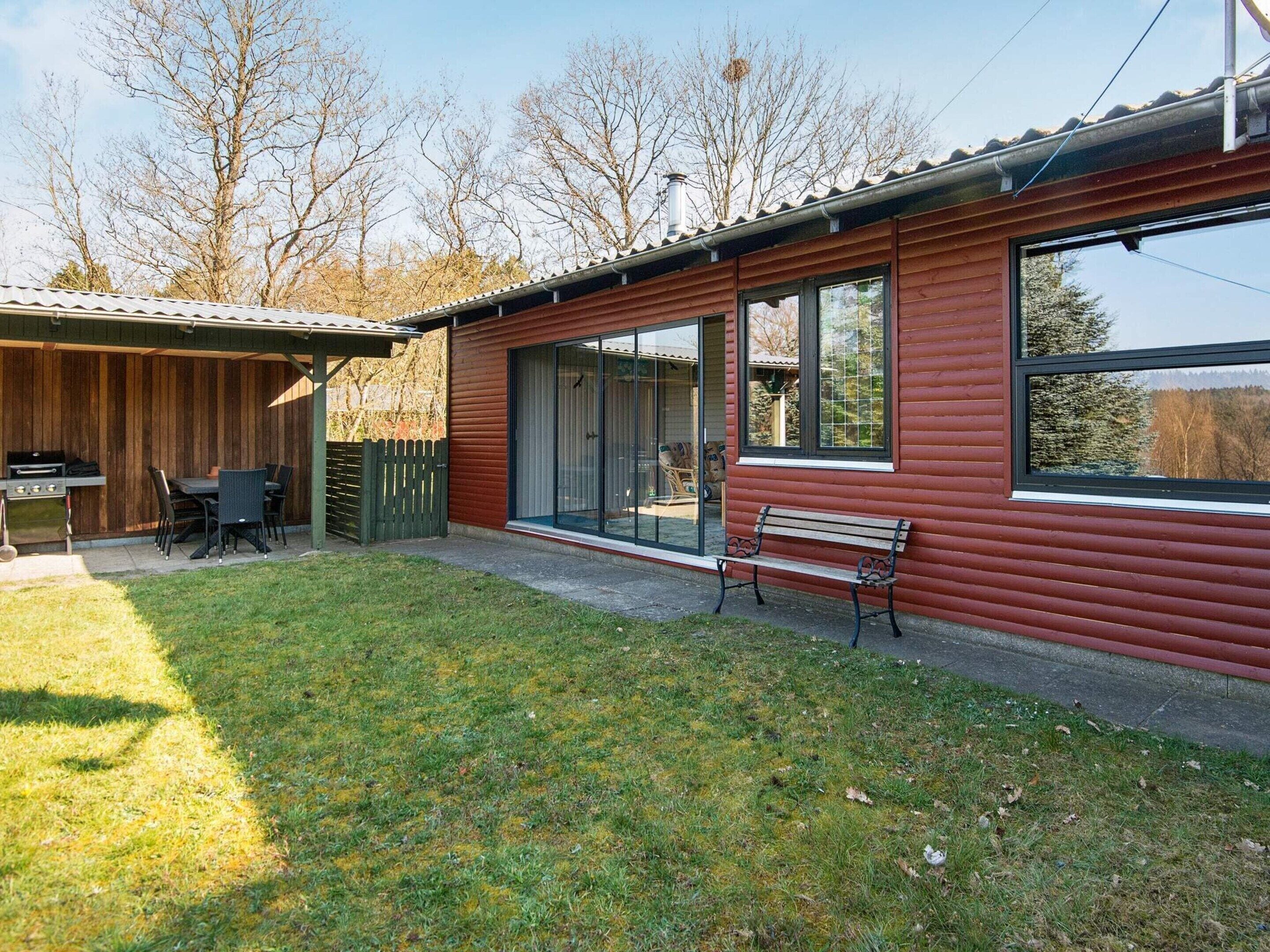 Une cabane en bois avec une terrasse, un barbecue et un banc.
