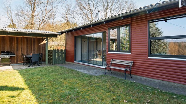 Eine Holzhütte mit einer Terrasse, einem Grill und einer Bank.