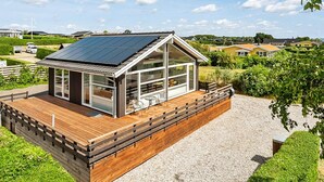 Een modern huis met een houten terras, grote ramen en een dak met zonnepanelen.