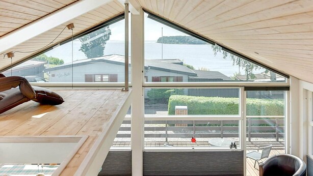 Een moderne loft slaapkamer met een schuine plafond, grote ramen en uitzicht op een steiger en water.
