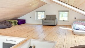 Slaapkamer met hoog plafond, houten vloeren, een bed, een stoel en twee ramen.