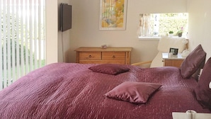A bedroom with a large bed, a wooden dresser, a chair, and a window with a view of greenery.