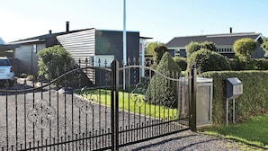 A gated entrance with a metal fence, a mailbox, and a modern building with a sloped roof.