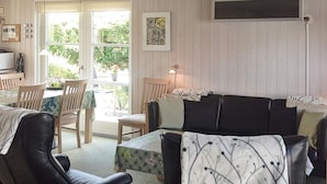 A living room with a black leather sofa, a dining table with chairs, and a window with a view of greenery.