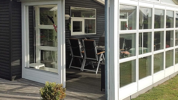 A house with a covered porch, a dining area with chairs, and a small garden with potted plants.
