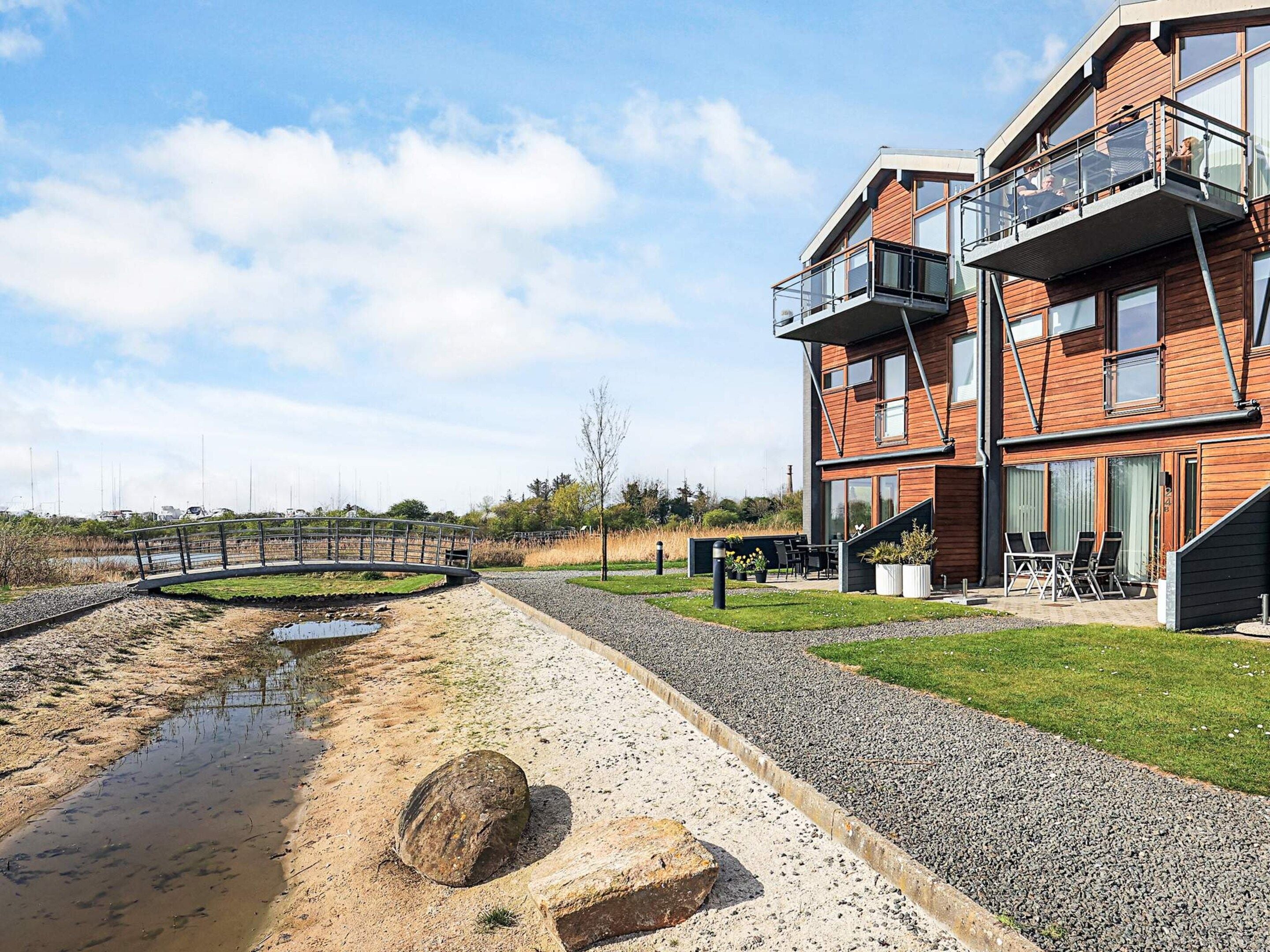A modern two-story building with a balcony, a gravel pathway, and a small water feature.