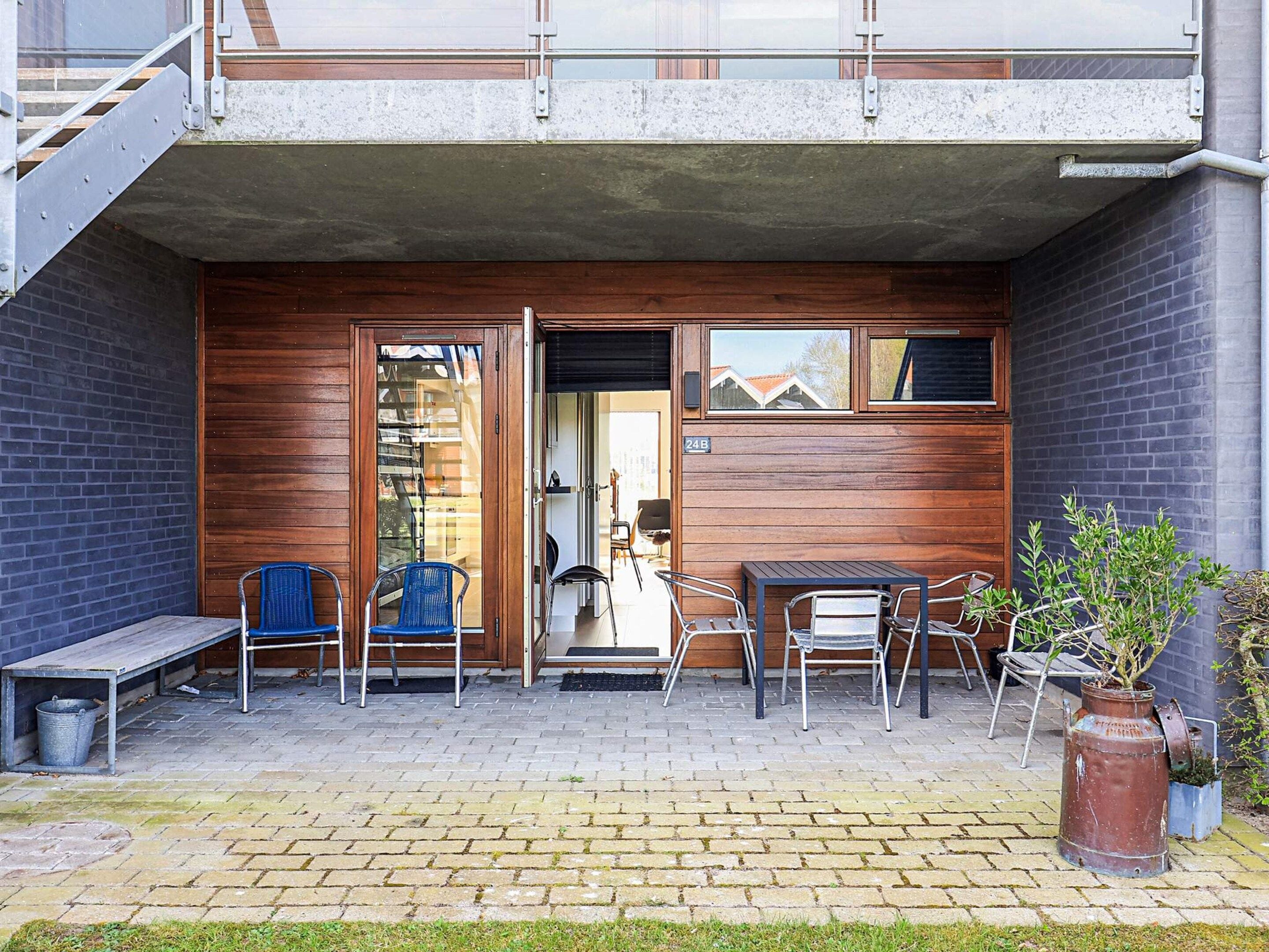 A building entrance with a wooden facade, a metal staircase, and a patio area with outdoor seating.