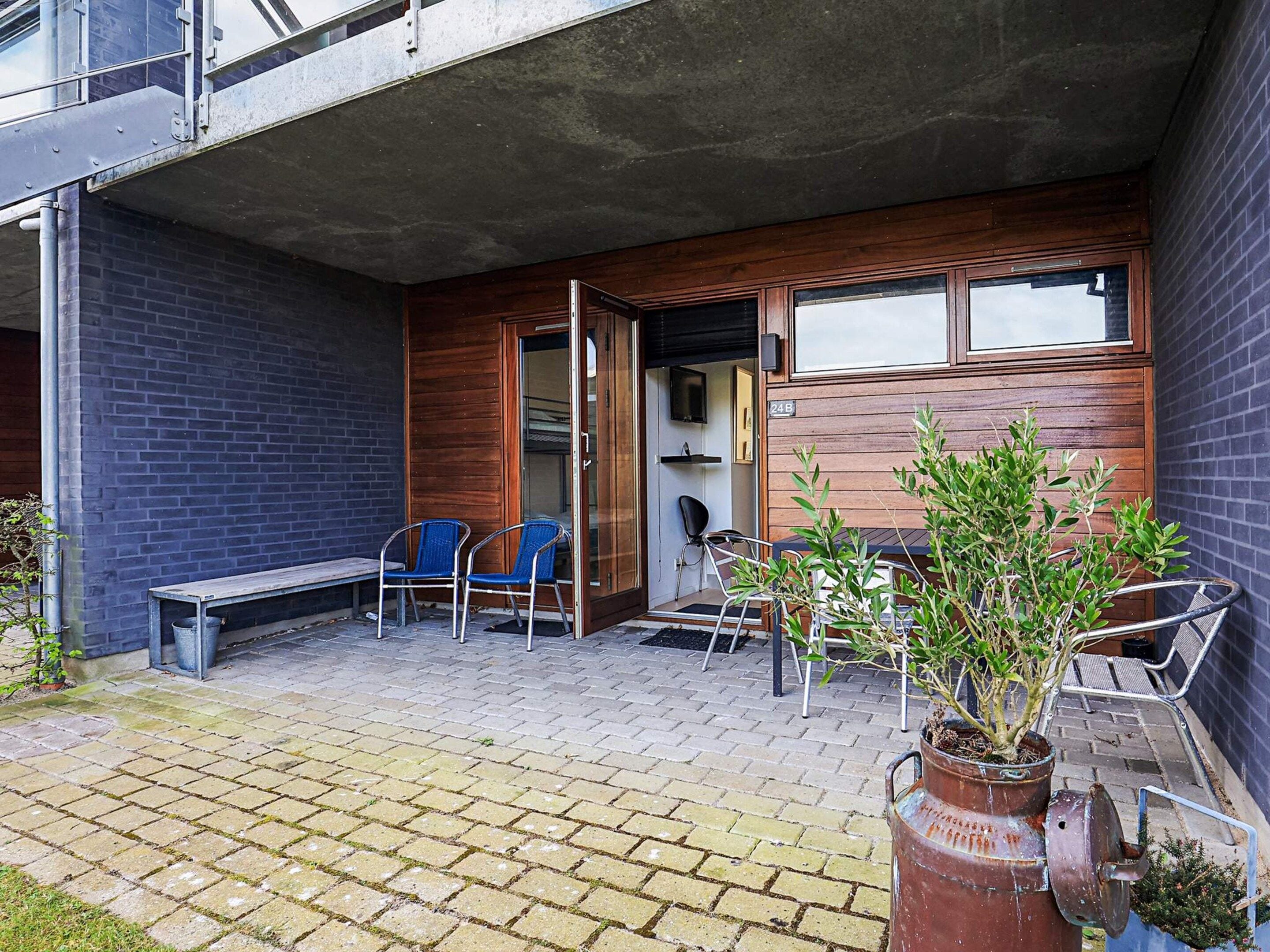 An outdoor patio with a bench, chairs, and potted plants.