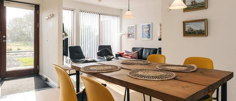 Un comedor con mesa de madera, sillas amarillas y individuales tejidas.