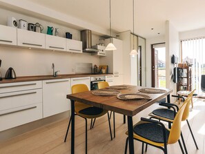 A modern kitchen with white cabinets, a wooden dining table with woven placemats, and a view of the outdoors through a glass door.