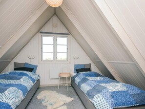 Un dormitorio pequeño y acogedor en el desván, con dos camas, un ventanal y una mesita.