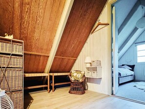 A loft bedroom with a sloped ceiling, wooden beams, a bed, a small table, and wicker baskets. - Lovely Holiday Home in Jutland near Sea (Ringkobing)
