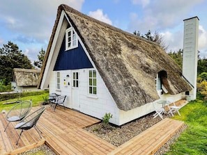 A thatched-roof house with a blue and white exterior, a wooden deck, and a small garden area. - Lovely Holiday Home in Jutland near Sea (Ringkobing)