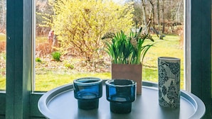 Una ventana con vistas a un jardín, una planta en maceta y tres candelabros azules sobre una bandeja.