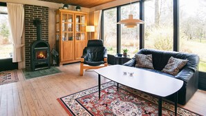 Una sala de estar acogedora con chimenea, un sofá de cuero, una mesa de madera y ventanas amplias que dan a vistas del exterior.