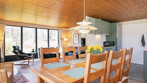 Un comedor con una mesa y sillas de madera, una lámpara colgante y vistas al exterior a través de amplios ventanales.