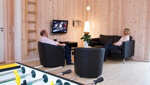 Een kamer met houten wanden, een televisie, twee banken en een tafelvoetbaltafel.