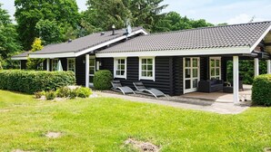 Une cabane en rondins avec un toit en tuiles, deux fauteuils et une terrasse couverte.