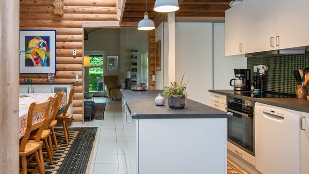 L’intérieur d’un chalet moderne en bois, avec une cuisine, un coin repas et une vue sur l’extérieur.
