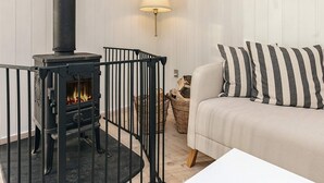 A cozy room with a black wood-burning stove, a white sofa with striped pillows, and a lamp against a white paneled wall. - 6 Person Holiday Home in Blokhus (Blokhus)