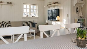 A living room with a sofa, two white chairs, a TV, and a kitchen area with a microwave. - 6 Person Holiday Home in Blokhus (Blokhus)