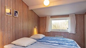 Ein Schlafzimmer mit einer Holzwand, einem Bett mit blauer Bettwäsche, einem Fenster mit Vorhängen und zwei Wandleuchten.