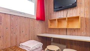 Ein Zimmer mit Holzwänden, einem an einer Holzhilfe montierten Fernseher, einem Schreibtisch, einem Stuhl und einem Fenster mit rotem Vorhang.