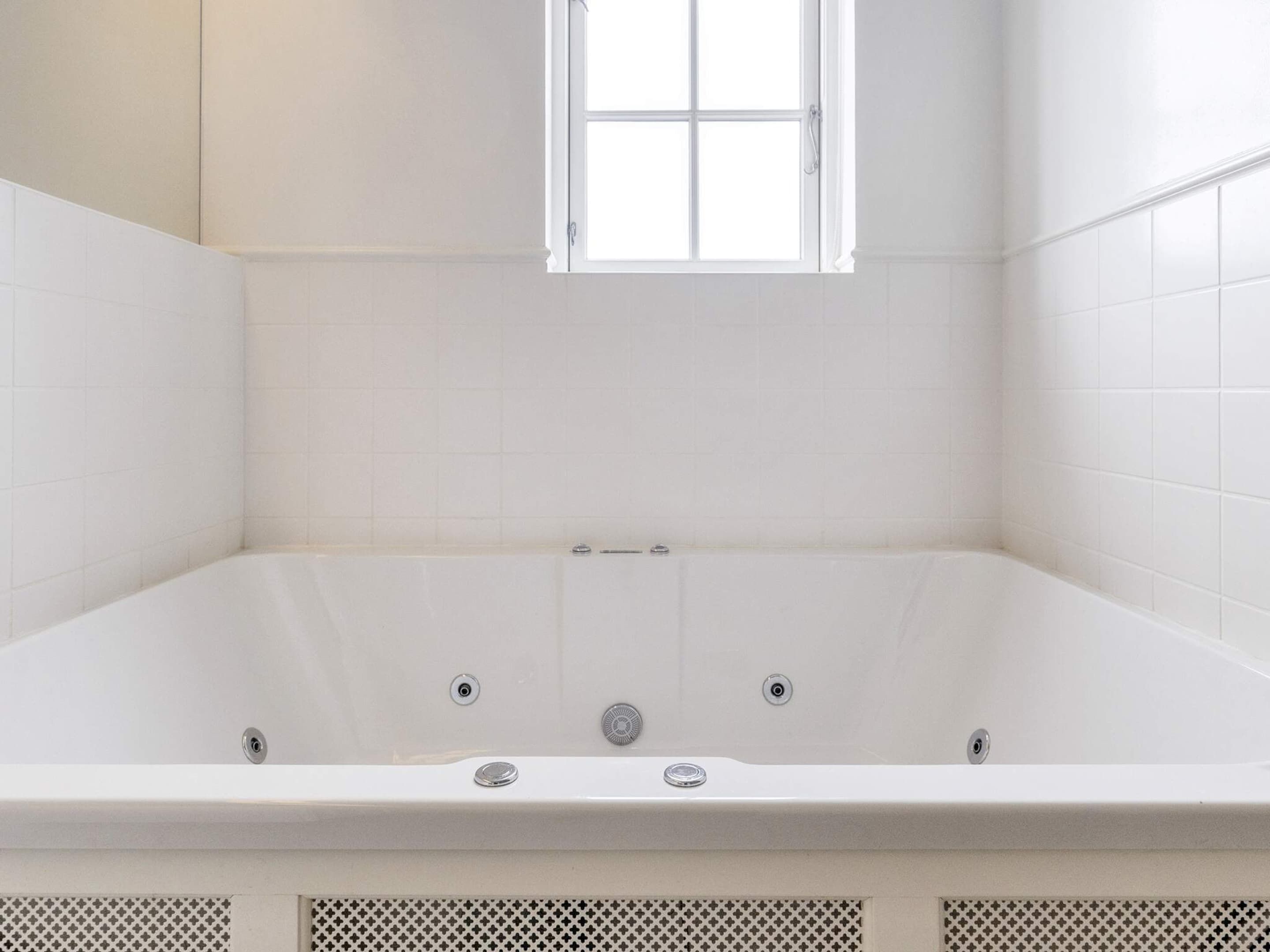 Un baño moderno con una bañera independiente, azulejos blancos y una ventana sobre la bañera.