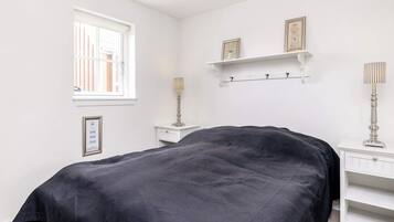 Un dormitorio con cama, mesita de noche, lámpara, ventana y estante con marcos de fotos.