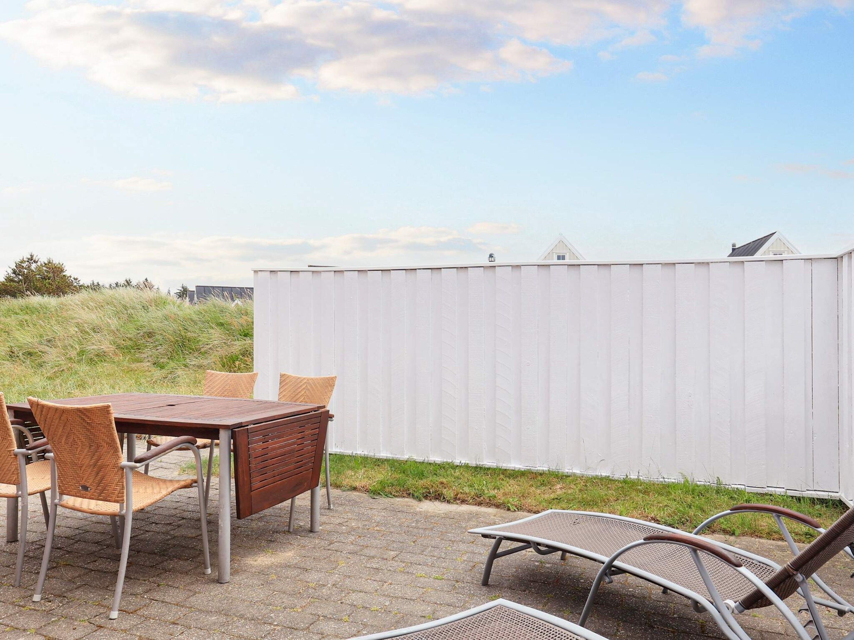 An outdoor patio with a table and chairs, a white fence, and a grassy area.