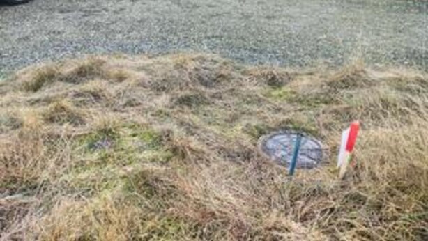 A grassy area with a manhole cover and a red and white sign.