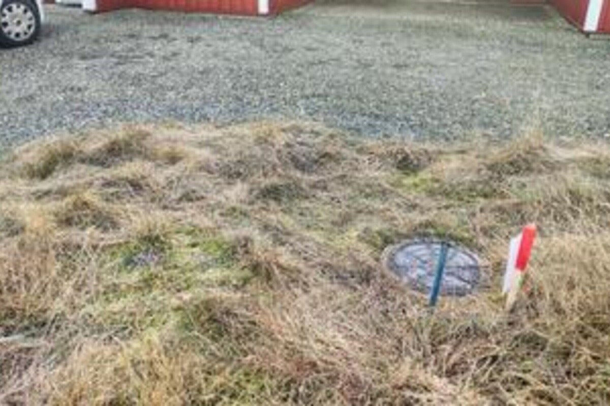 A grassy area with a manhole cover and a red and white sign.