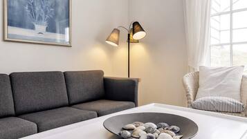 A modern living room with a grey sofa, a white coffee table with seashells, a floor lamp, and a wicker chair with cushions.