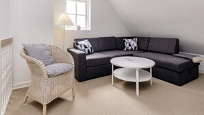 A modern living room with a sectional sofa, a wicker chair, a round coffee table, and a floor lamp. - 5 Star Holiday Home in Blokhus (Blokhus)