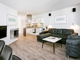 Un espacio moderno para vivir con sofá, mesa de centro y una zona de cocina al fondo.