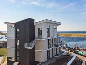A modern multi-story building with a balcony, large windows, and a view of a marina with boats. - Holiday Home in Wendtorf (Schönberg)