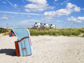 A beach chair with a flag, a sandy beach, and a building with multiple balconies in the background.
