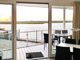 Una habitación con puerta de vidrio corredera que da a un balcón con vista al agua y un barco. Hay una mesa y sillas en el balcón.