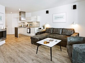 A modern living room with a sectional sofa, a coffee table, and a kitchen area in the background. - Holiday Home in Wendtorf (Schönberg)